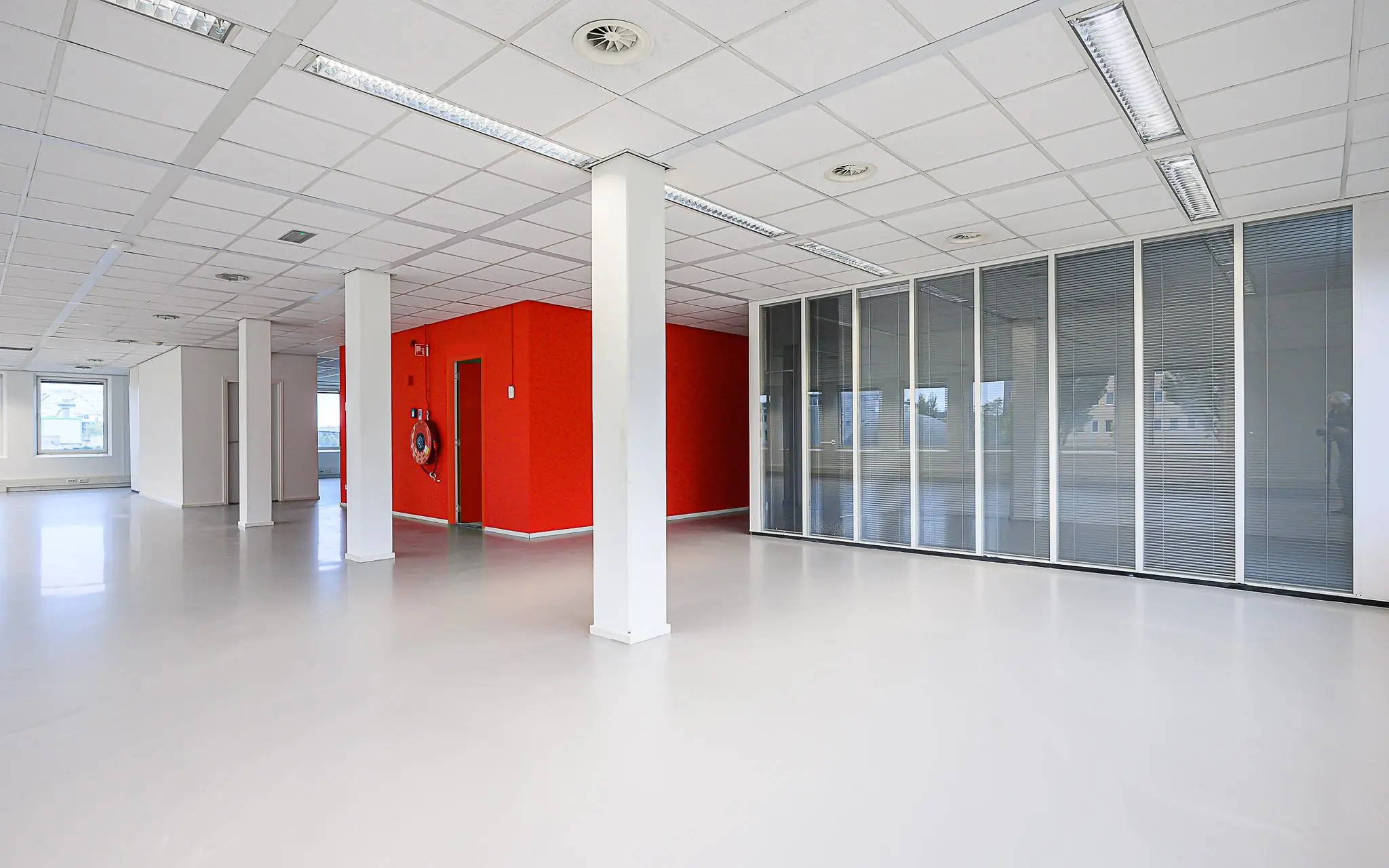 Lichte, moderne kantoorruimte aan de Rivium Westlaan met glazen scheidingswanden en een felrode accentmuur.